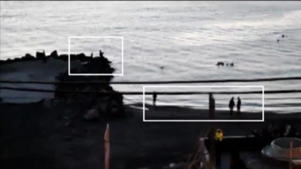 Fotograma del vídeo grabado por ATLAS. En la imagen, y dentro del recuadro blanco, agentes de la Guardia Civil en la orilla de la playa de El Tarajal apuntando con sus escopetas a los migrantes que tratan de llegar a nado. Les dispararon con balas de goma.